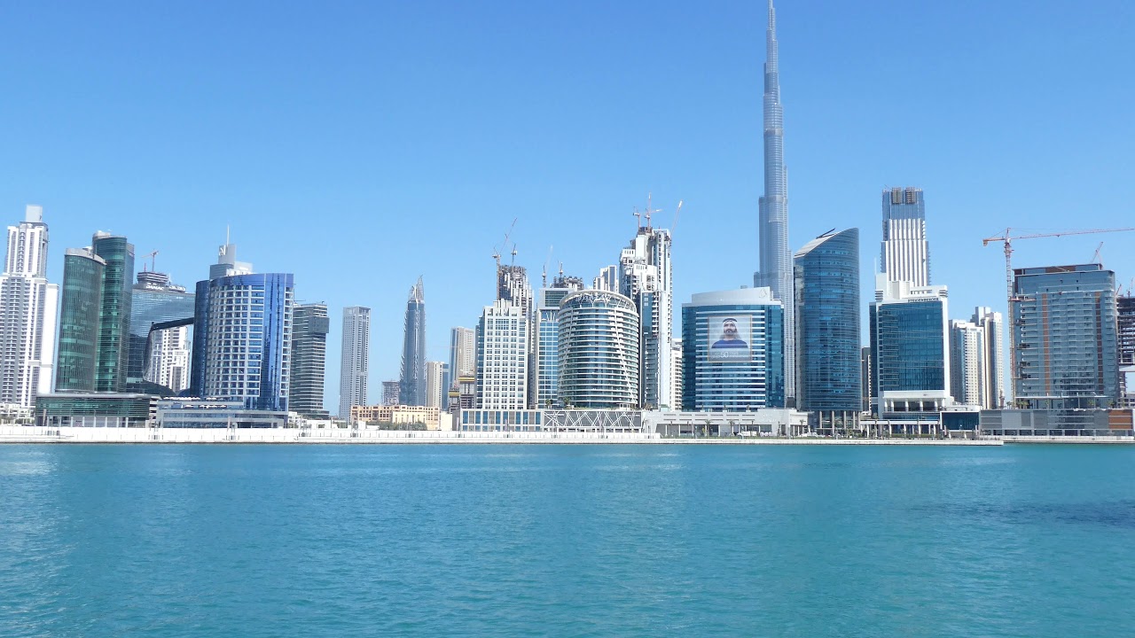 Aerial split-view comparison of Downtown Dubai Burj Khalifa and Dubai Fountain against Business Bay’s canal waterfront and modern high-rise towers, highlighting the urban contrast between luxury tourism and business living.