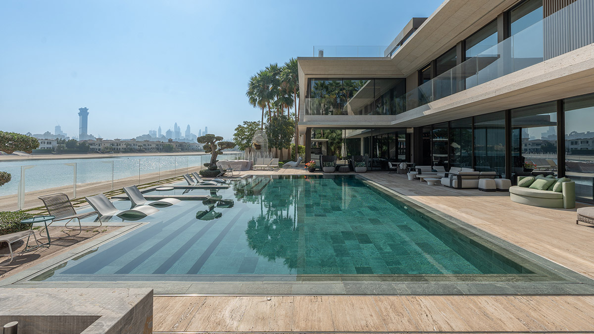 Aerial drone shot of the Palm Jumeirah coastline showcasing luxury villas, crystal-clear waters, and the Dubai skyline.